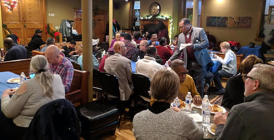 Community gathering — diverse group of people seated around tables in a community center, engaged in conversation and fellowship.